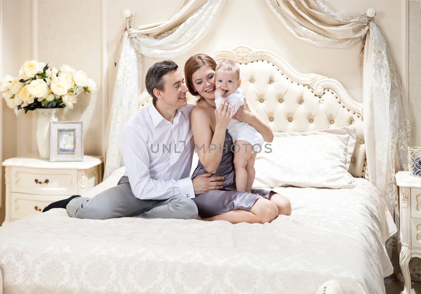 Young happy family with a baby on bed by photobac
