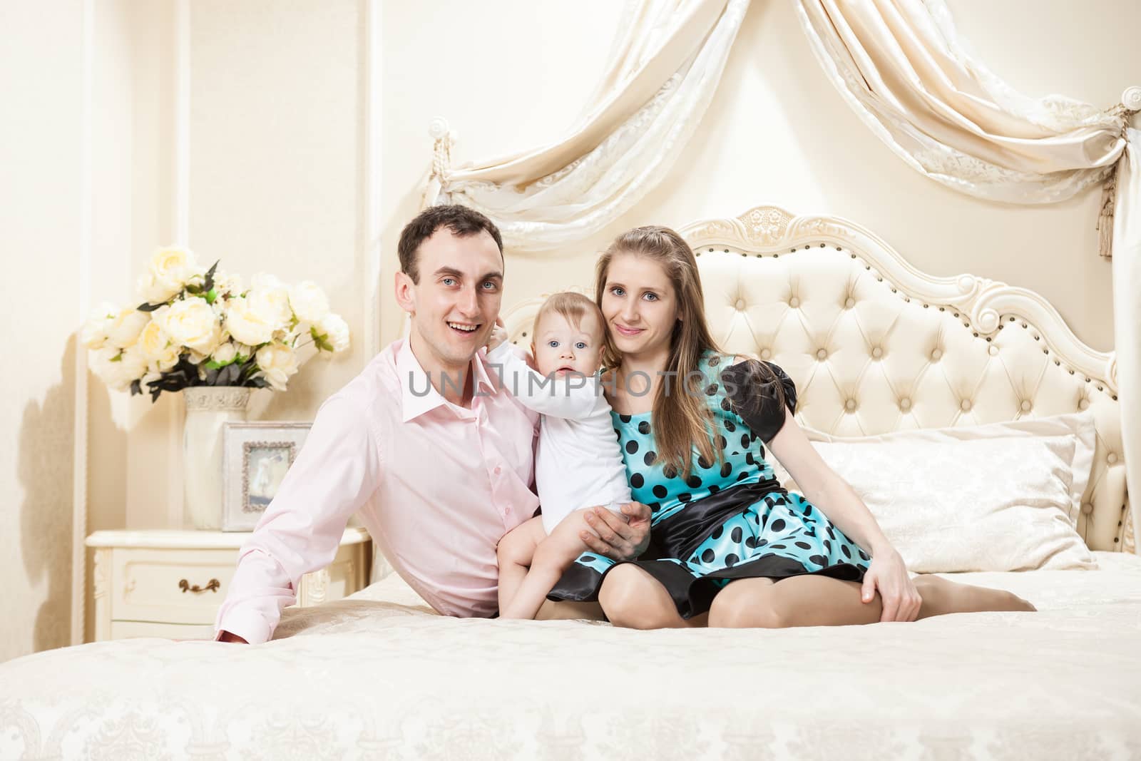 Young happy family with a baby on bed by photobac