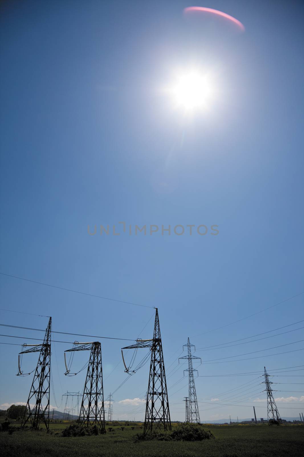 pillars with electricity transmitting lines in field under blue skies