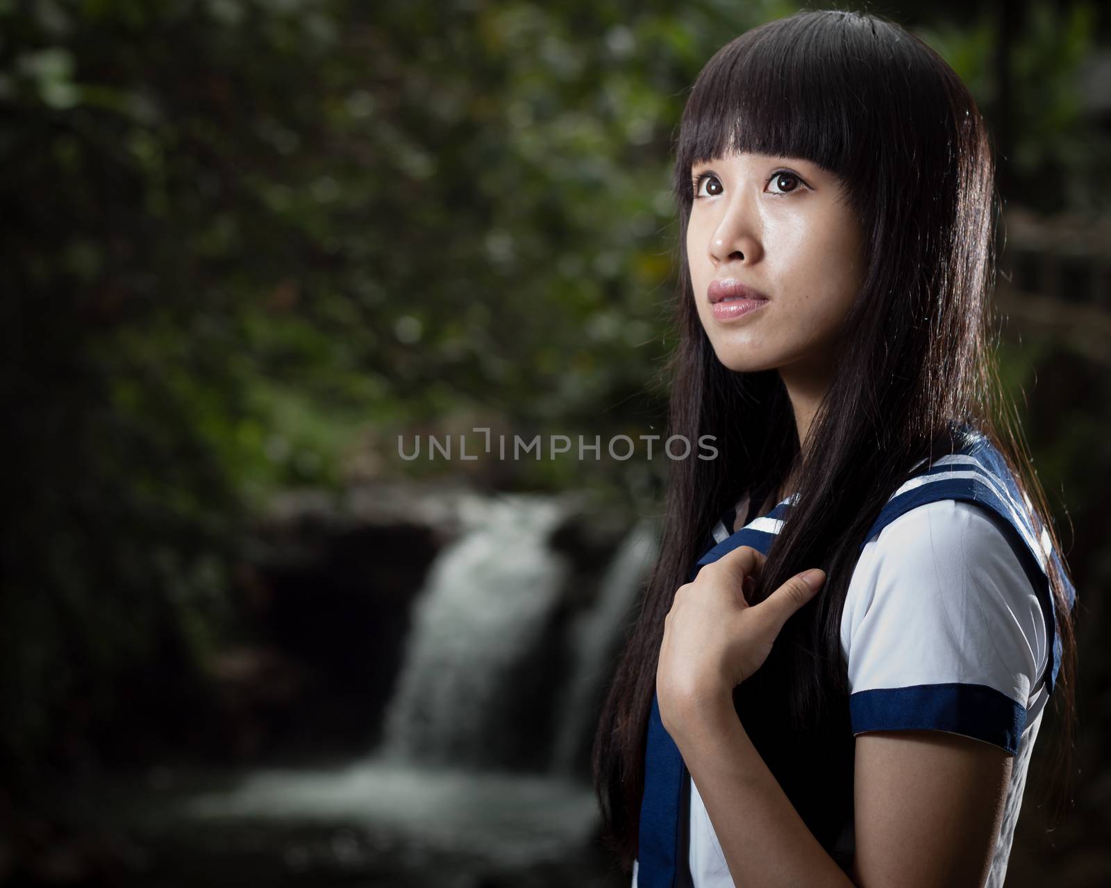Asian schoolgirl standing in front of waterfall by imagesbykenny