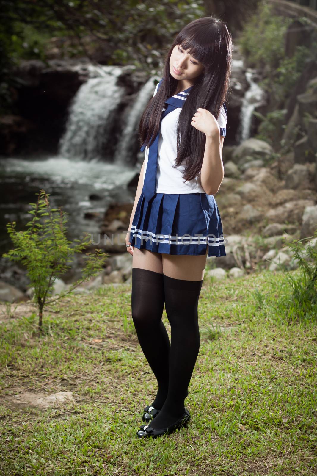 Asian schoolgirl standing in front of waterfall by imagesbykenny