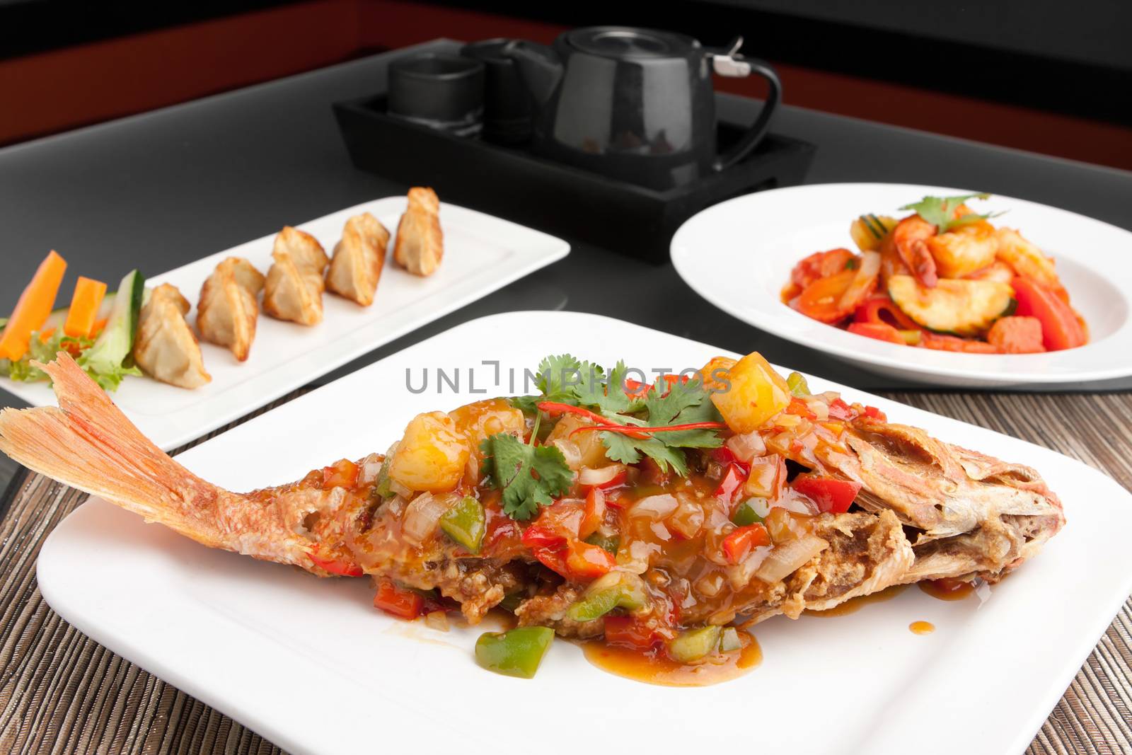 Freshly prepared Thai style whole fish red snapper dinner with sweet and sour shrimp and pan fried gyoza dumplings appetizer.  