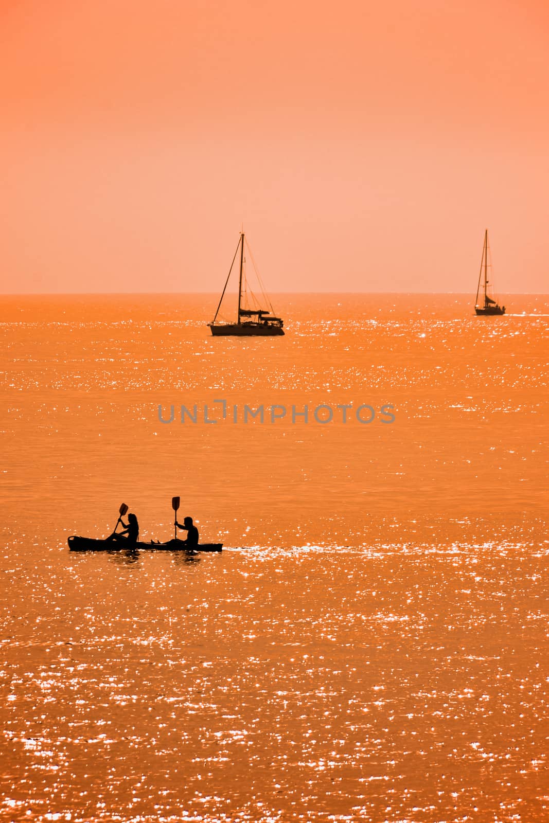 Kayak and two sailboats at sunset