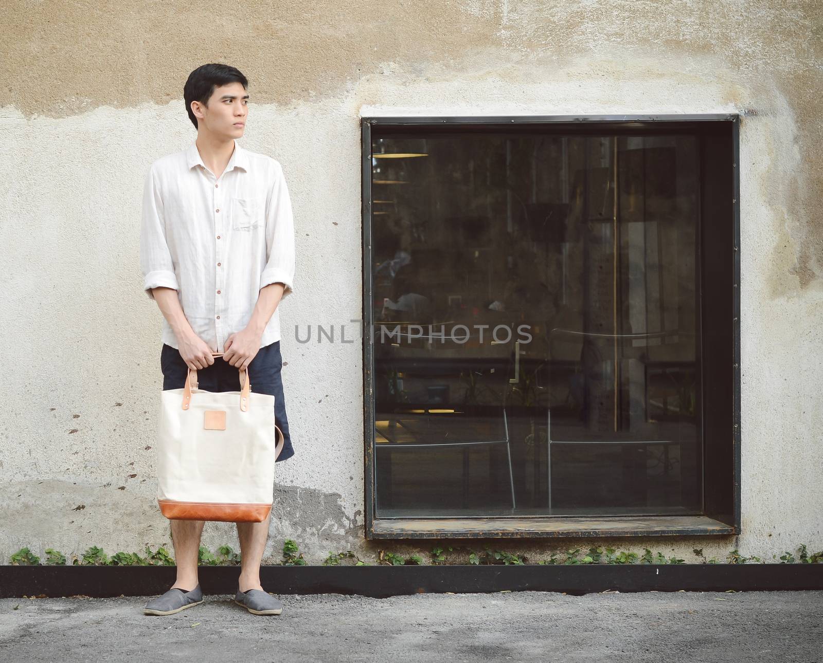 Attractive man with canvas bag on grunge concrete wall by siraanamwong