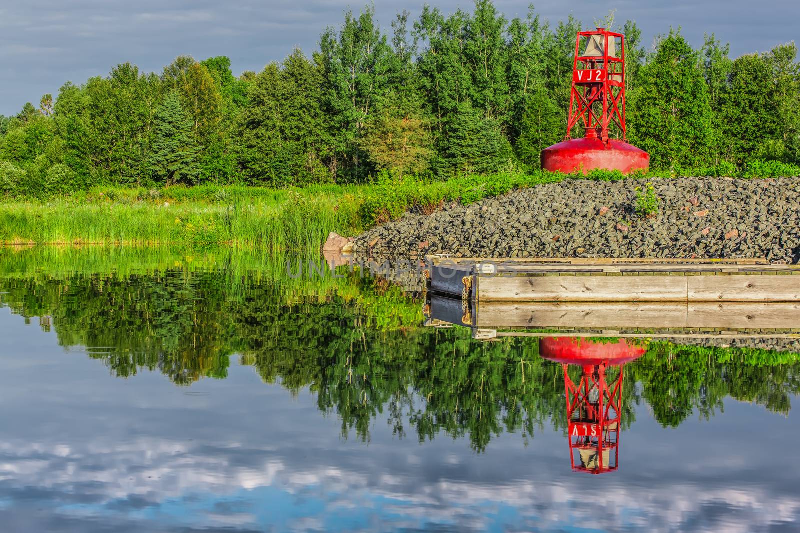 An abandoned red buoy on dry land by a lake and a dock in Ontario, Canada.