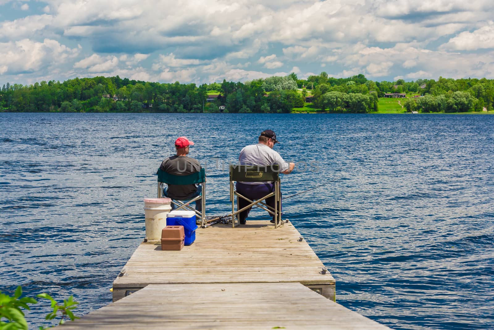 Two fishernem sitting and fishing in a lake.