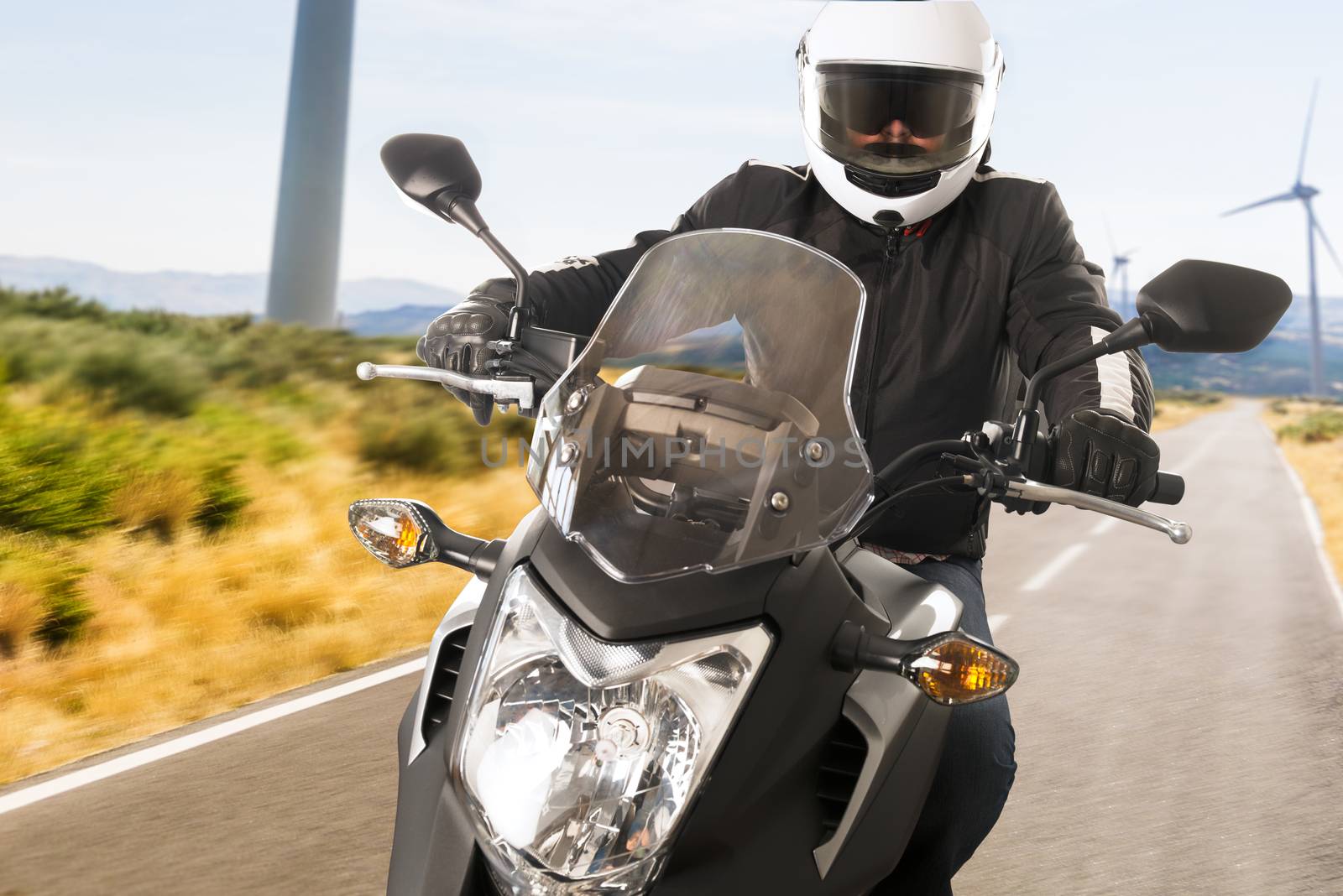 Biker in helmet and leather jacket riding on the road.