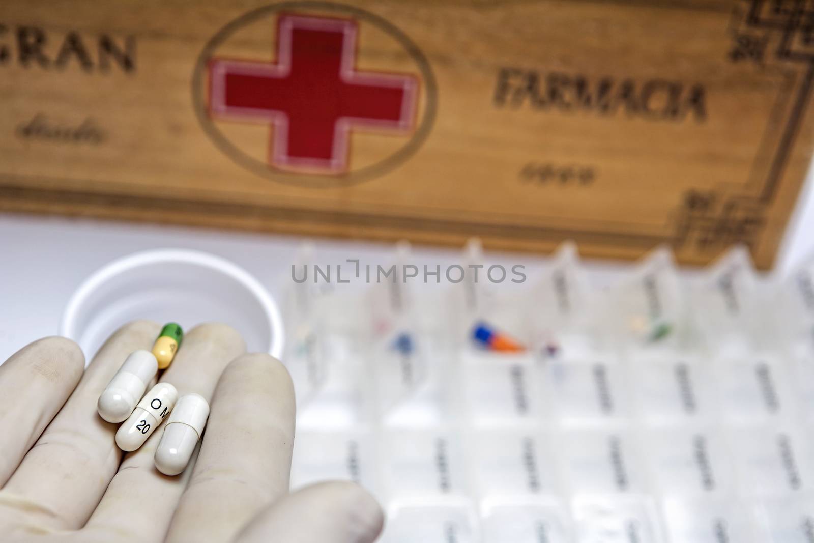 Hand with glove of white latex supports several tablets for classification, Pills with pill organizer next to old wood kit