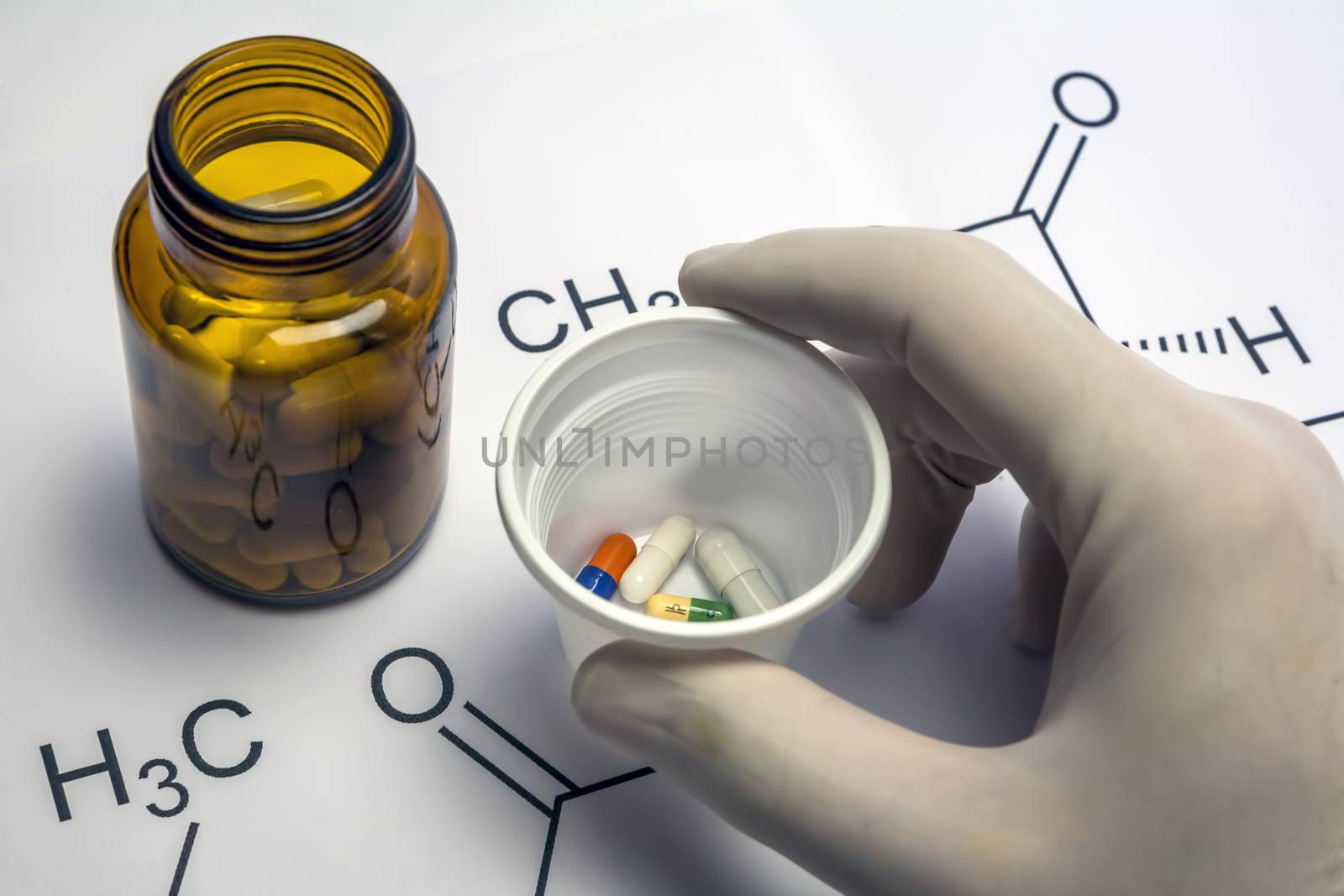 Hand with blue white glove holding white plastic cup with several pills