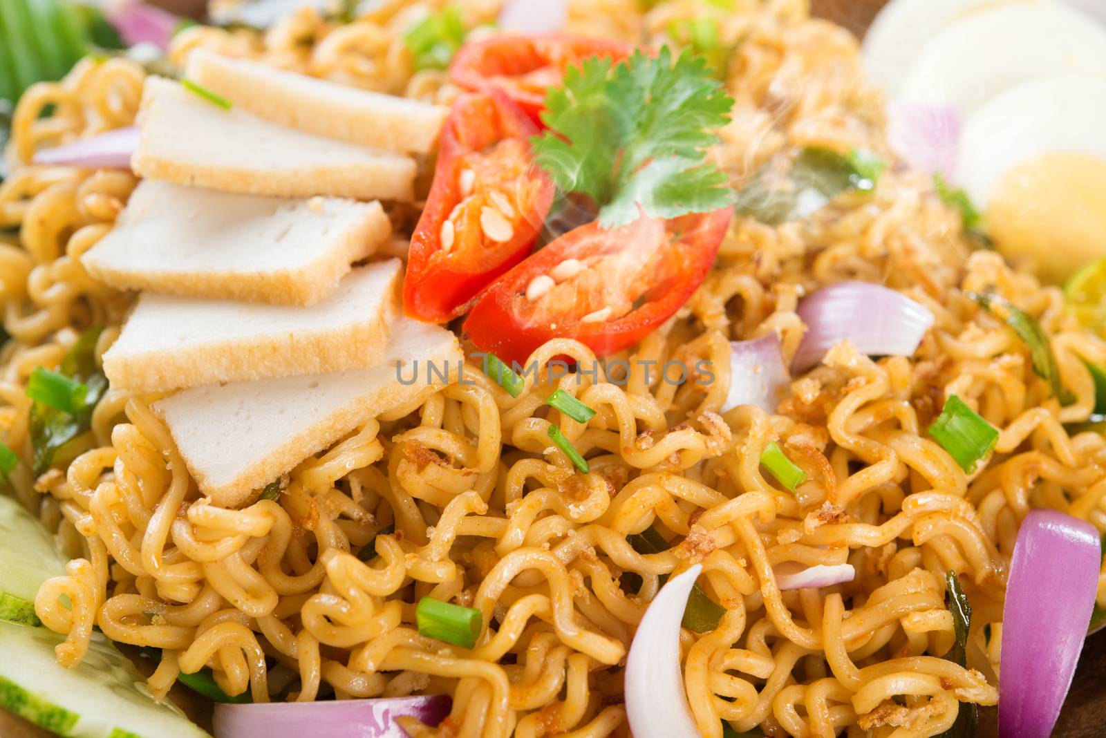 Close up Dry Instant Noodle, Malaysian style maggi goreng mamak or spicy dry curry instant noodles. Asian cuisine, ready to serve on wooden dining table setting. Fresh hot with steamed smoke.