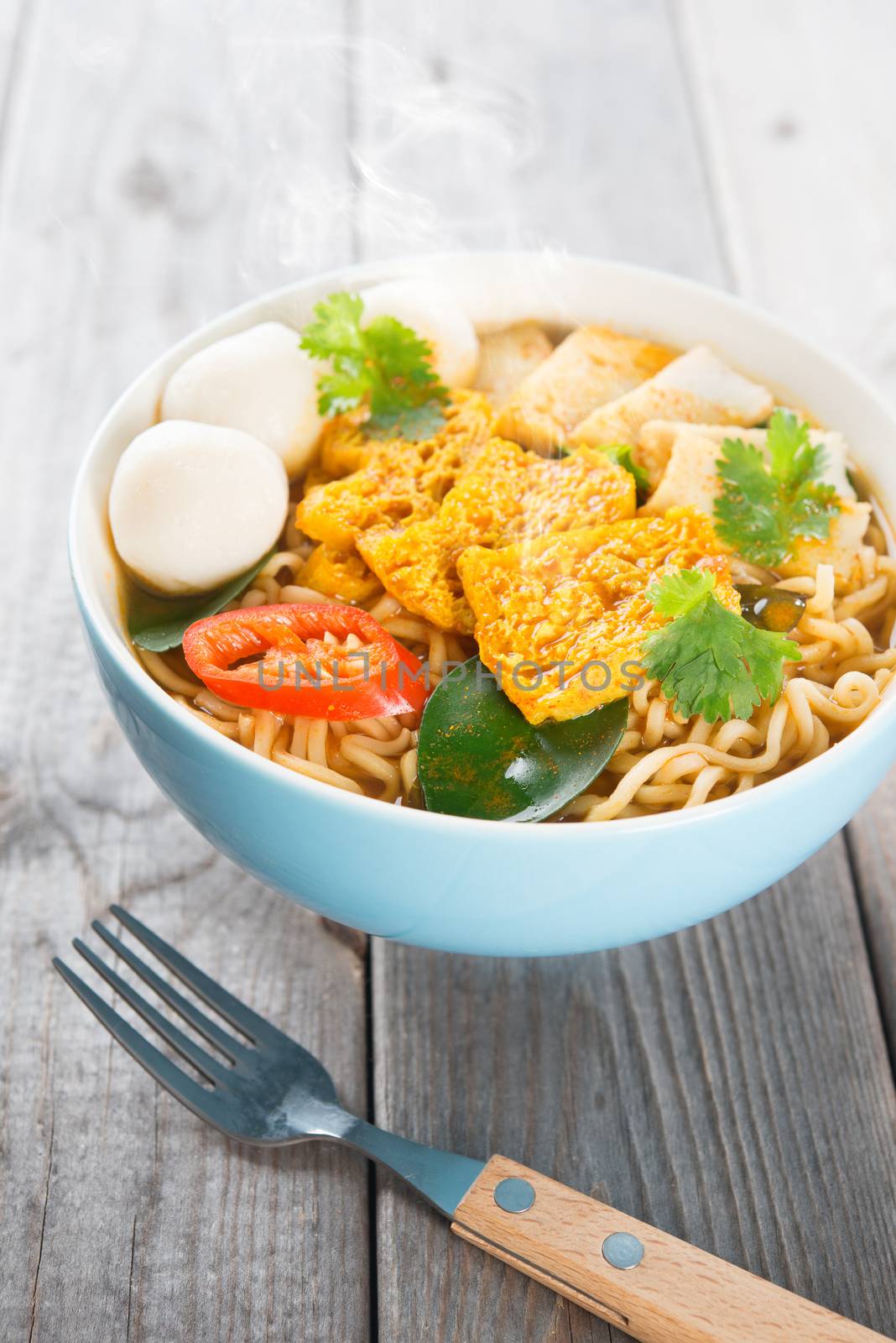 Spicy curry instant noodles soup with fork on wooden dining table. Fresh cooked, hot with steamed smoke.