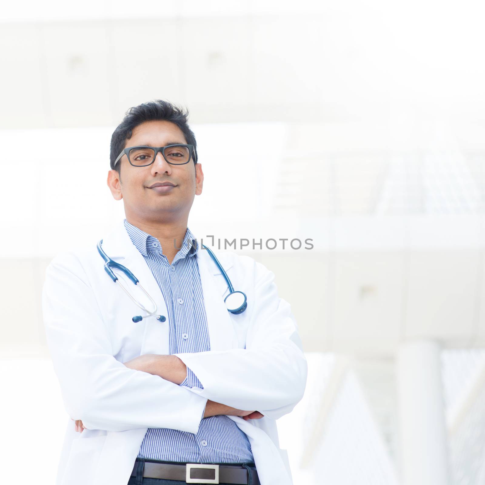 Portrait of a smiling Asian Indian male medical doctor in lab uniform standing in front of hospital.