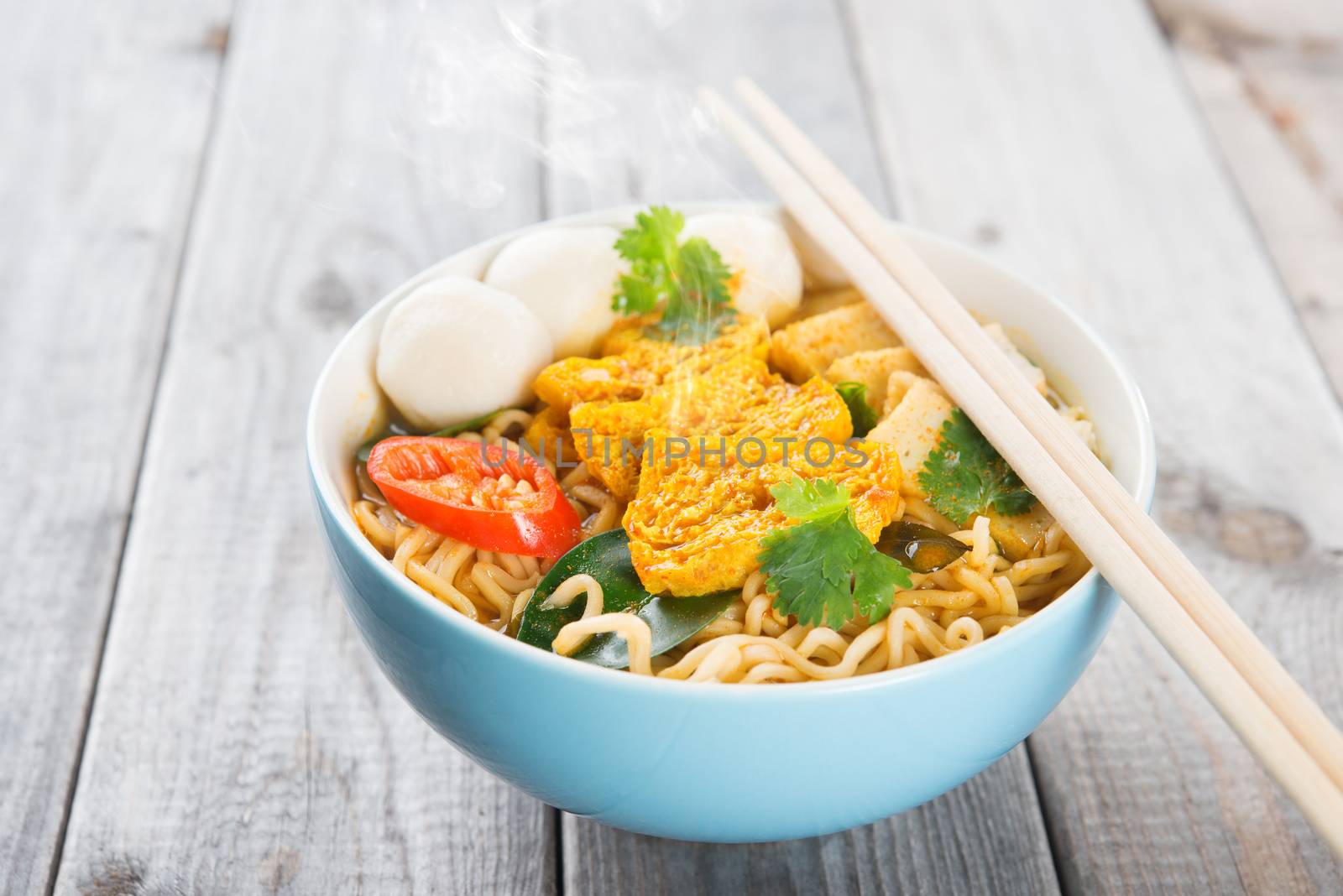 Spicy curry instant noodles soup with chopsticks on wooden dining table. Fresh cooked, hot with steamed smoke.