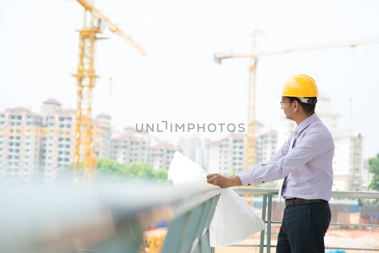 Portrait of a smiling Asian Indian male contractor engineer with hard hat inspecting at construction site.