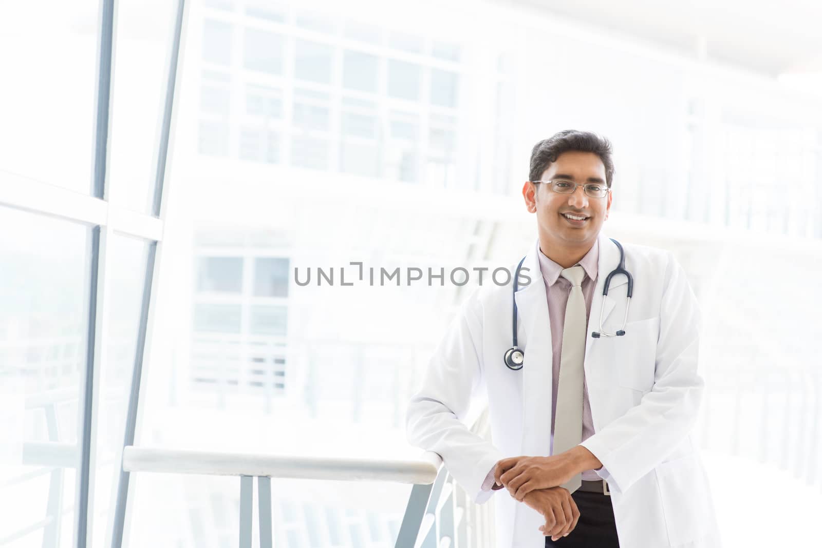 Portrait of a smiling Asian Indian male medical doctor standing inside hospital.