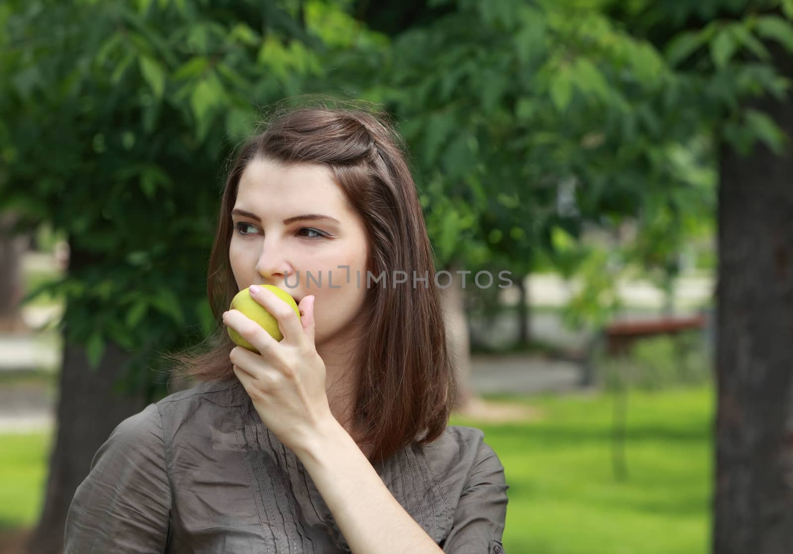 Portrait of a young woman biting in a fresh green apple outdoor in a park.