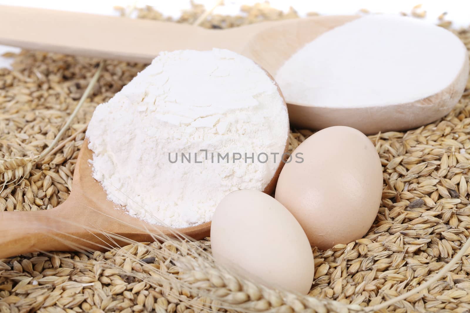 Spoon with flour on wheat background.