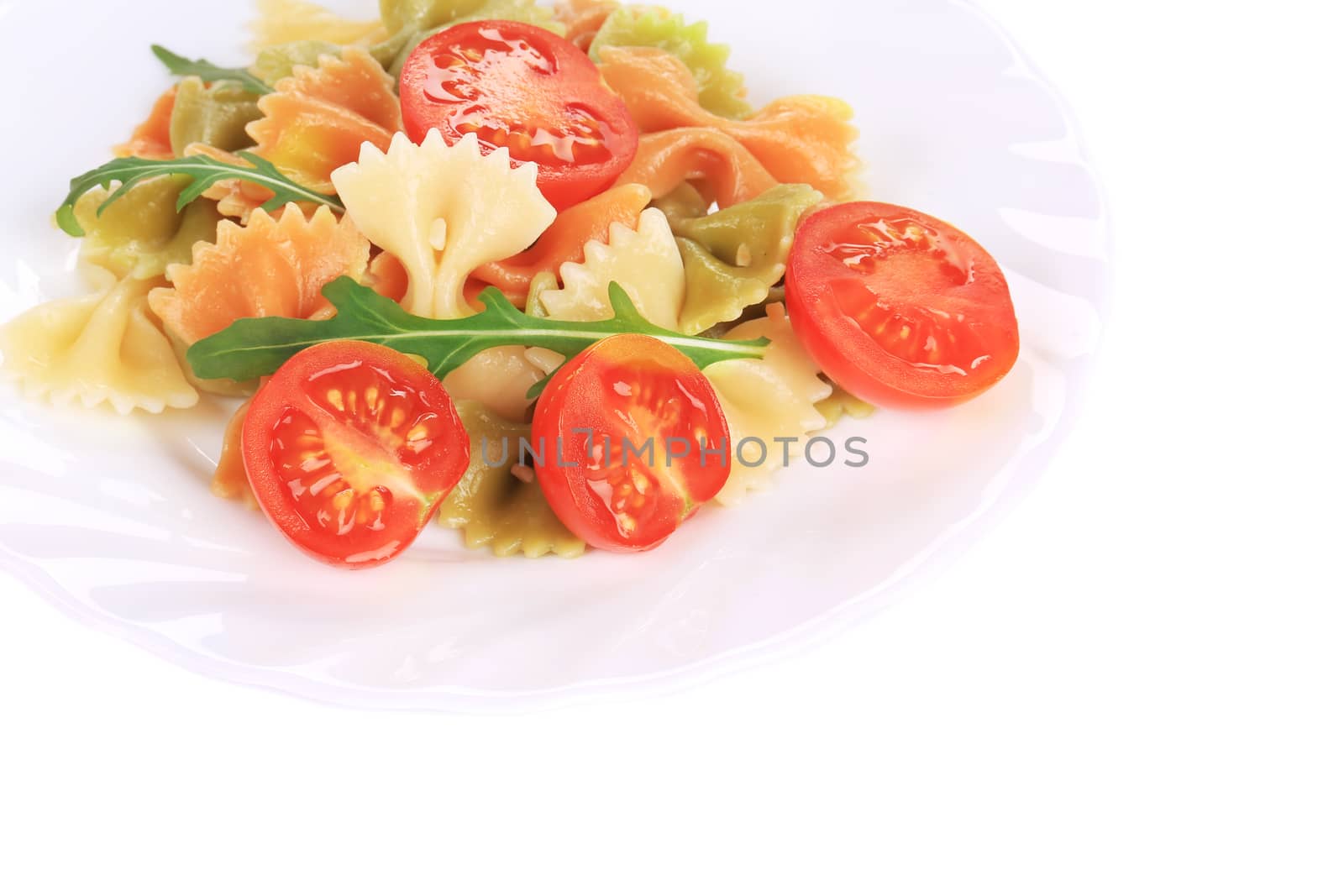 Colored farfalle on white plate with tomatoes. Whole background.