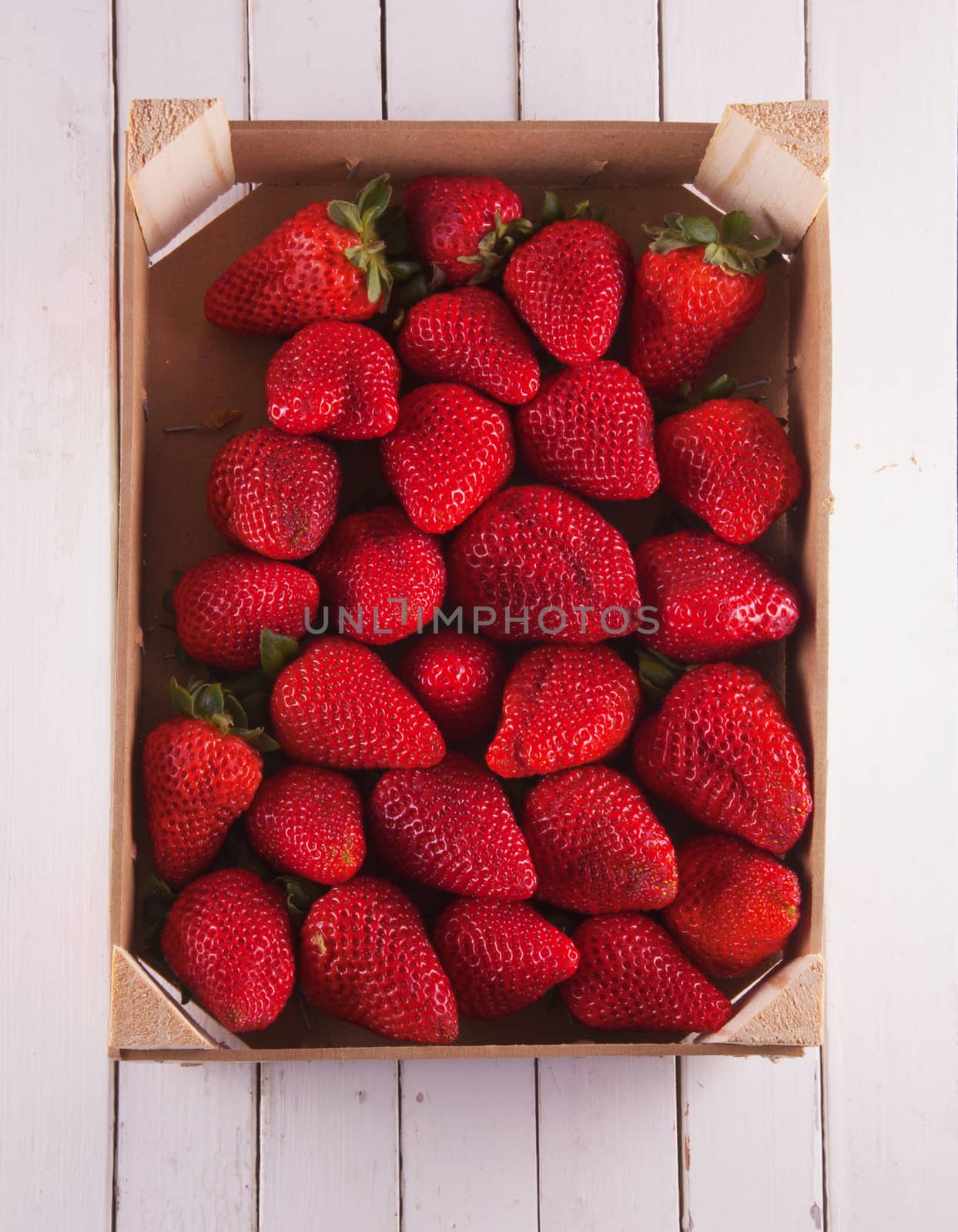 Strawberries in a box, over white wood, vertical image