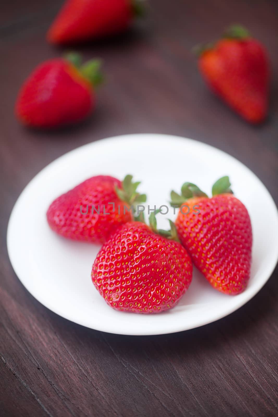 red juicy strawberry in a plate on a wooden surface