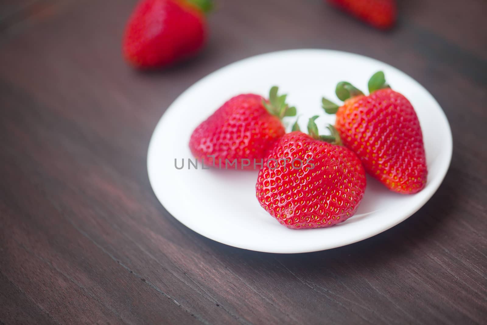 red juicy strawberry in a plate on a wooden surface by jannyjus