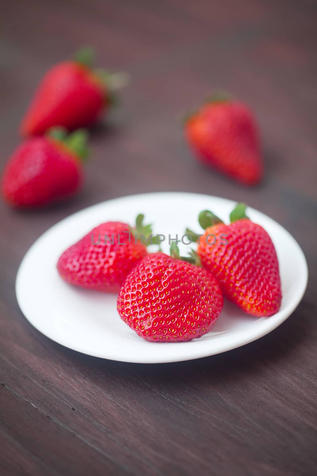 red juicy strawberry in a plate on a wooden surface by jannyjus