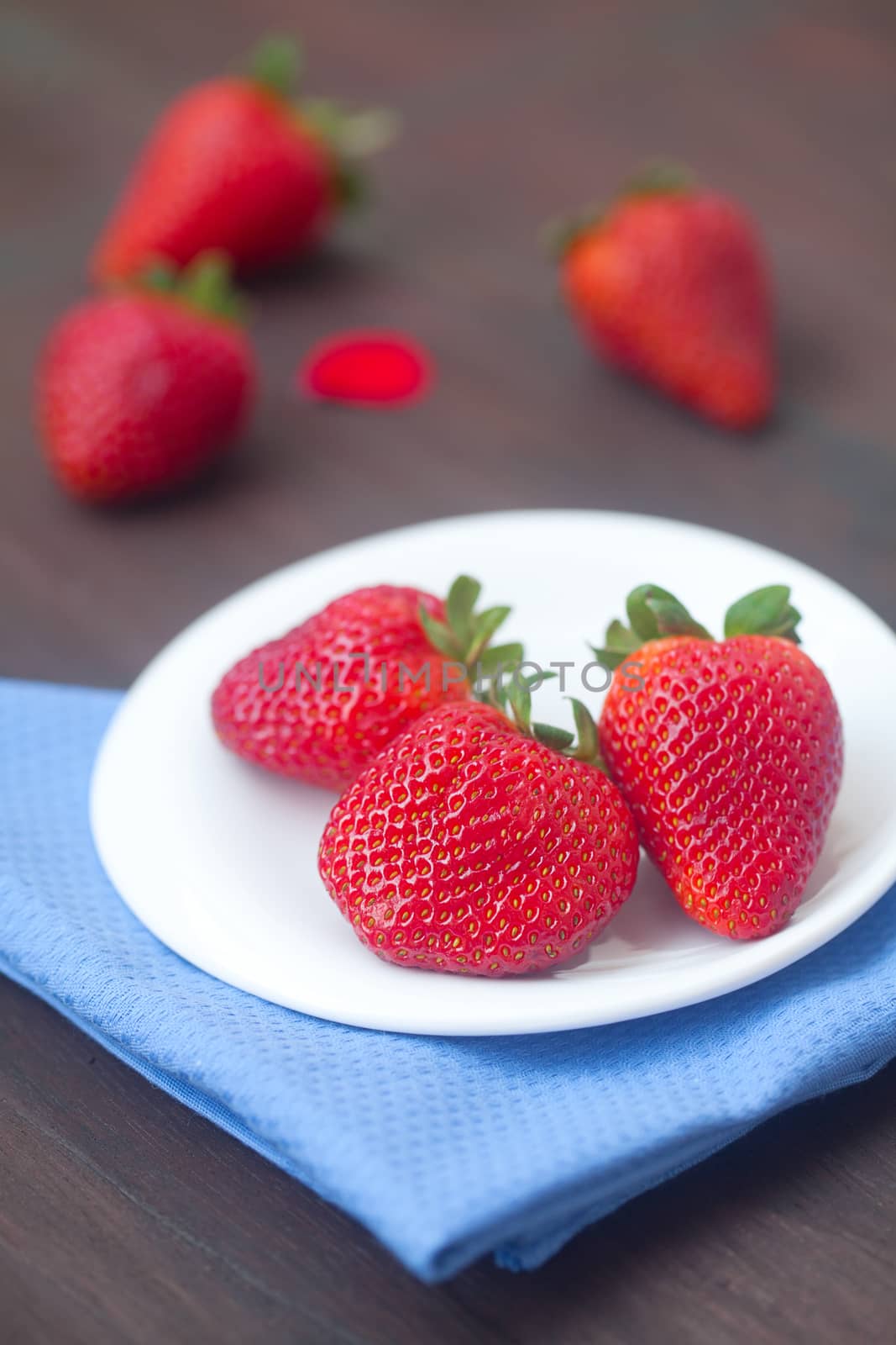 red juicy strawberry in a plate on a wooden surface by jannyjus