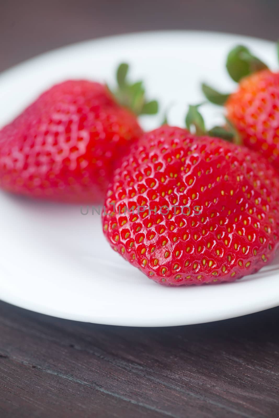 red juicy strawberry in a plate on a wooden surface by jannyjus