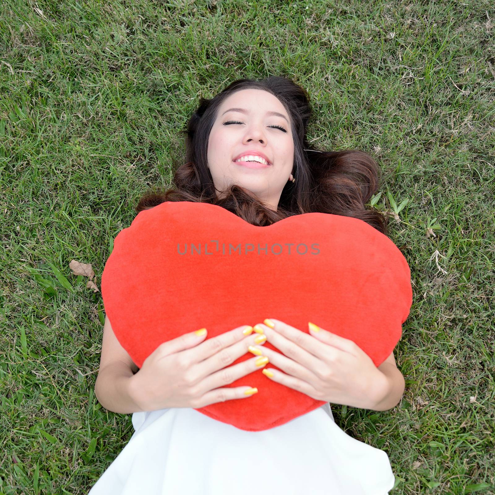 Women holding big love heart shape pillow on green grass by jakgree
