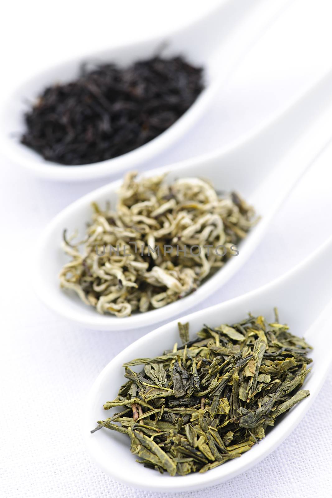 Black, white and green dry tea leaves in spoons