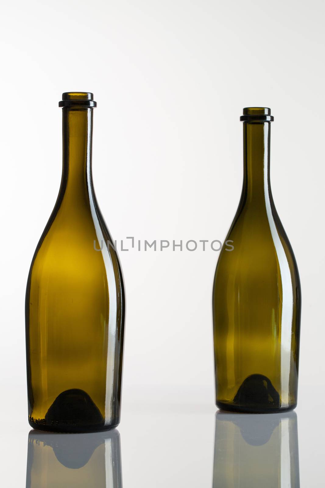 Two empty bottles of wine on a glass table by CaptureLight