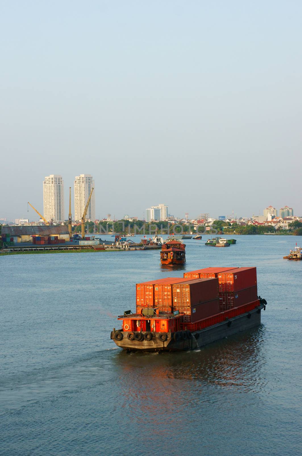 HO CHI MINH CITY, VIET NAM- MARCH 12: Maritime transport on river, vessel loading container on water, residential and apartment at riverside, scene of industrial city, Vietnam, March 12, 2014