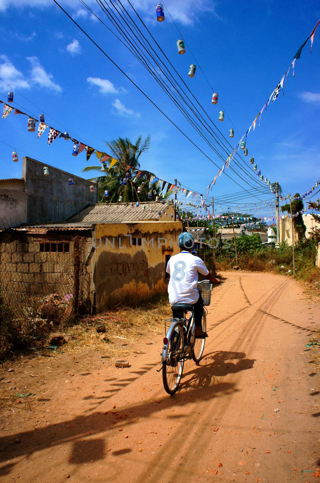 BINH THUAN, VIET NAM- JAN 21: Unidentified children riding bicycle on red soil path of poor Vietnamese countryside under blue sky on day, young boy riding bike alone to coming home, Vietnam, Jan 21, 2014