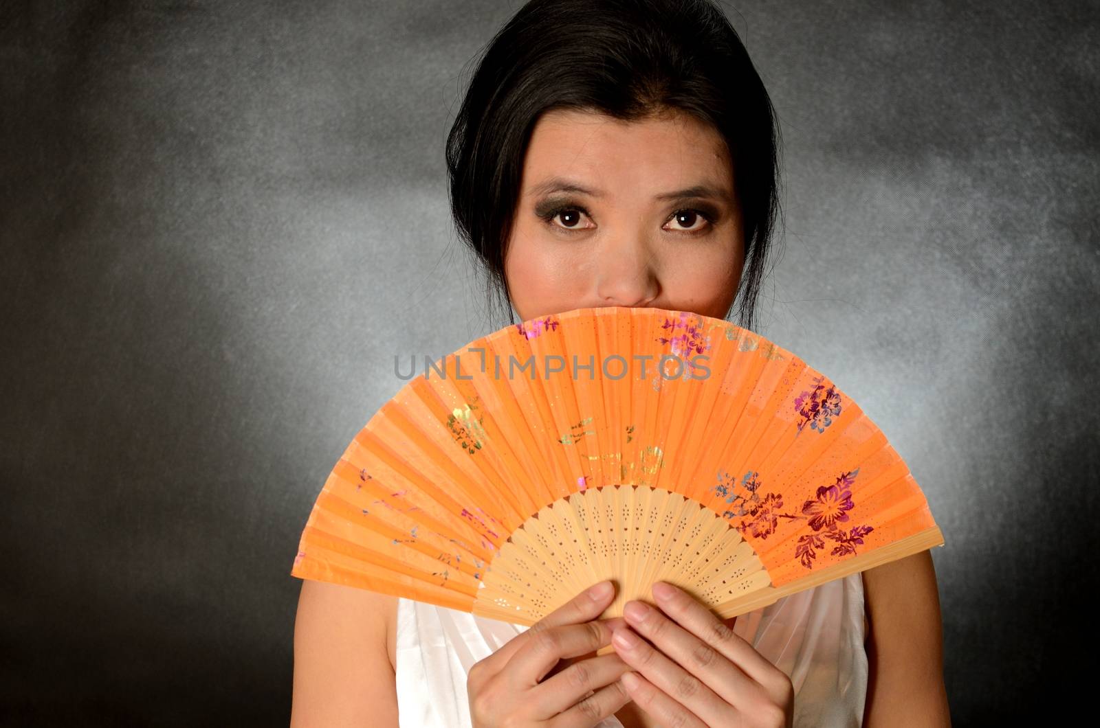 Asian female model wearing white dress. Young Chinese girl holding fan in hand, smiling gently.