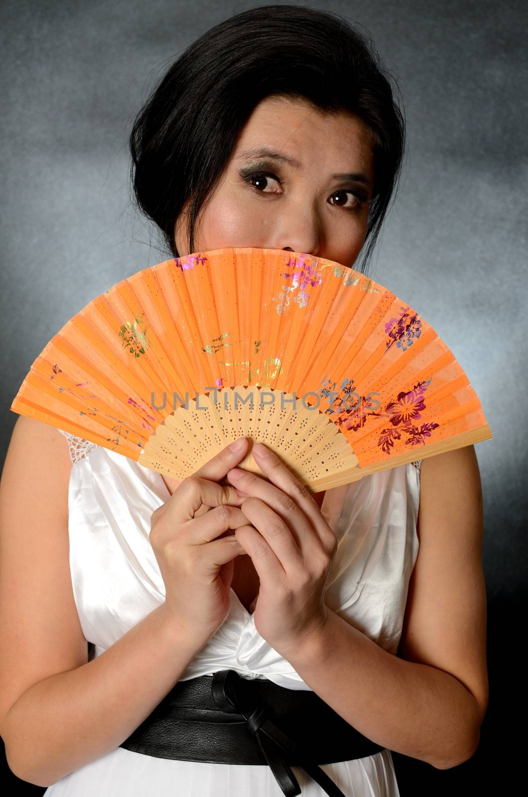 Asian female model wearing white dress. Young Chinese girl holding fan in hand, smiling gently.