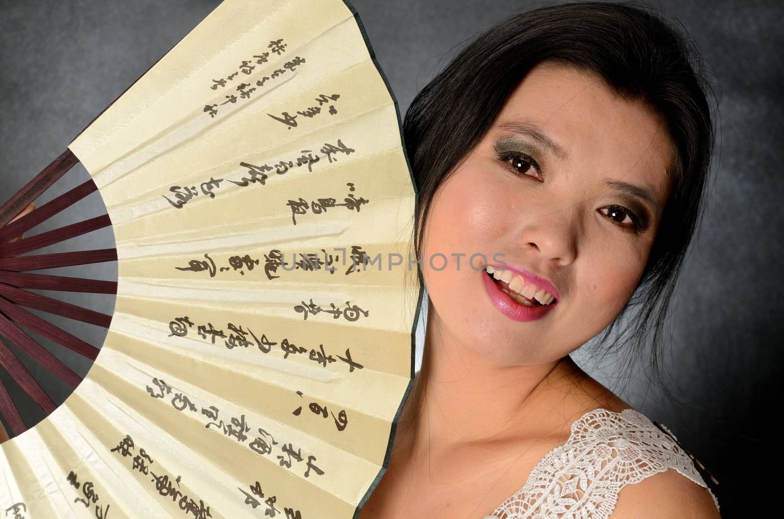 Asian female model wearing white dress. Young Chinese girl holding fan in hand, smiling gently.