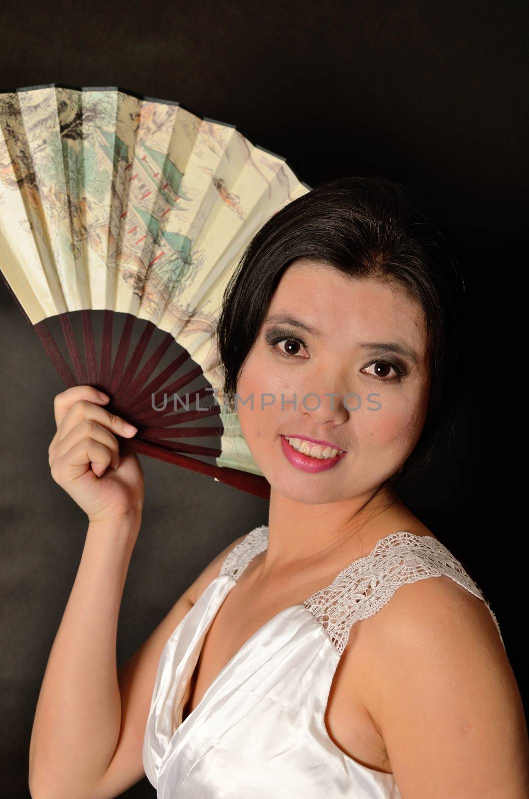 Asian female model wearing white dress. Young Chinese girl holding fan in hand, smiling gently.