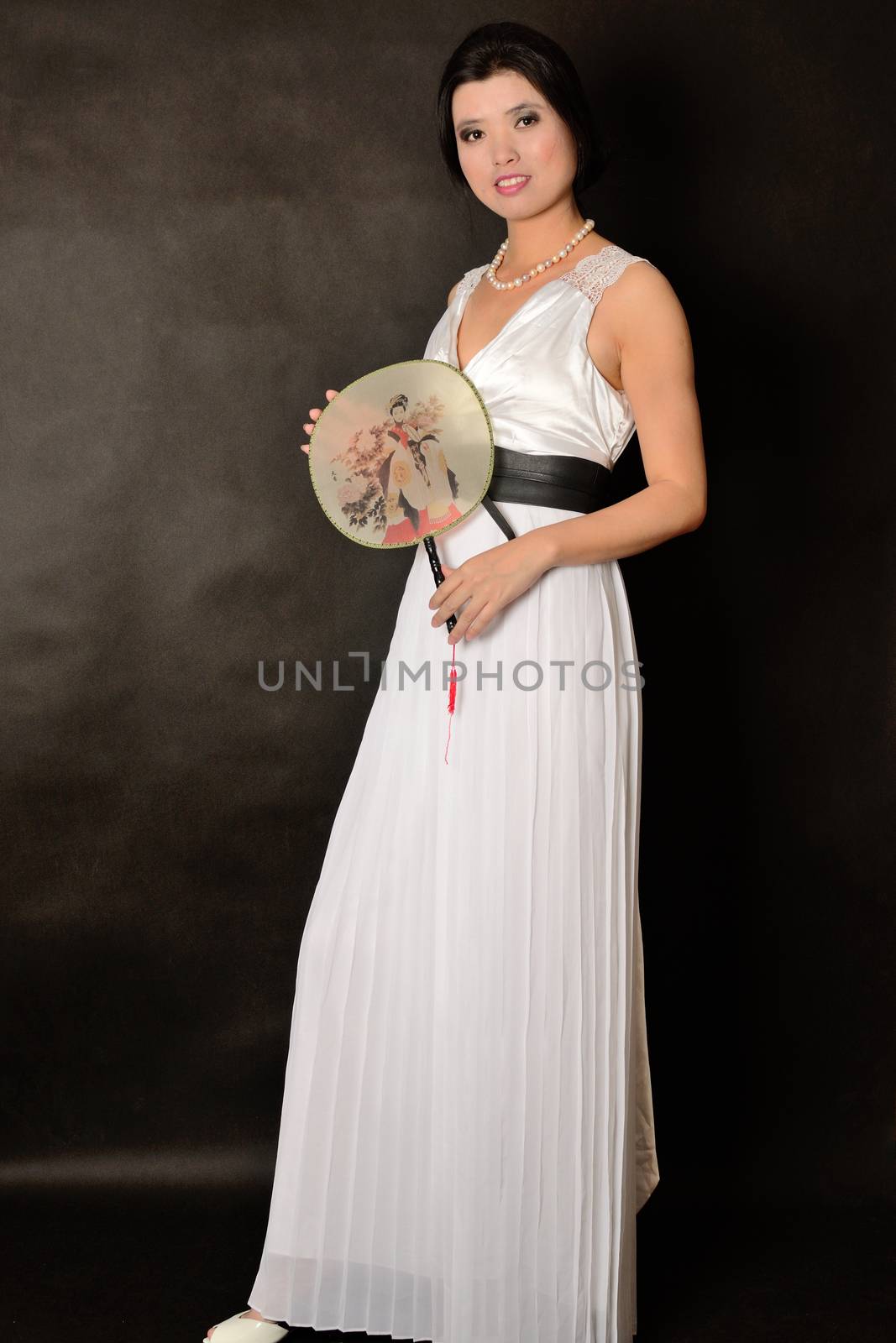 Chinese female wearing long white dress. Asian girl holding fan in her hand, girl with gentle smile.