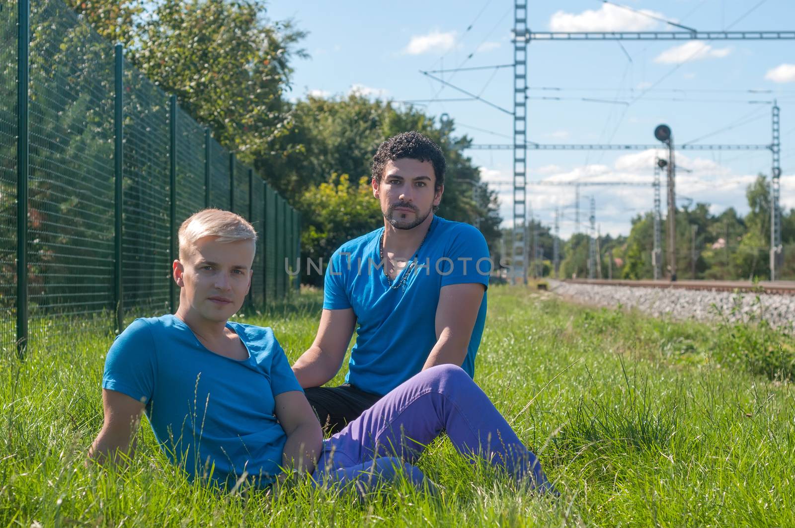 Two guys an in blue t-shirts sitting in a grass