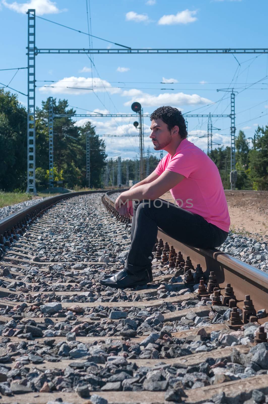 One man in pink t-shirt sitting on train tracks by anytka