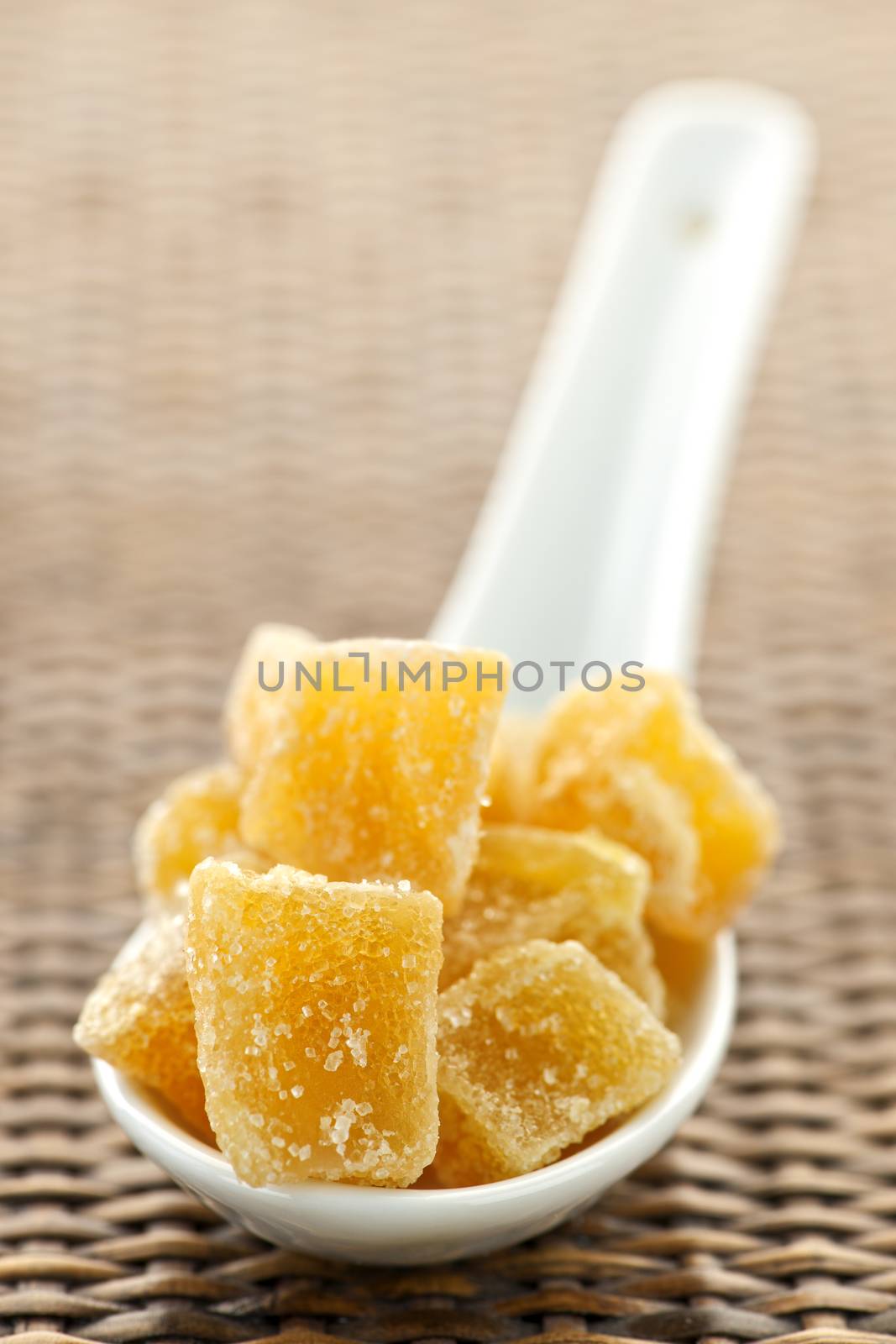 Caramelized ginger candy pieces on white spoon close up
