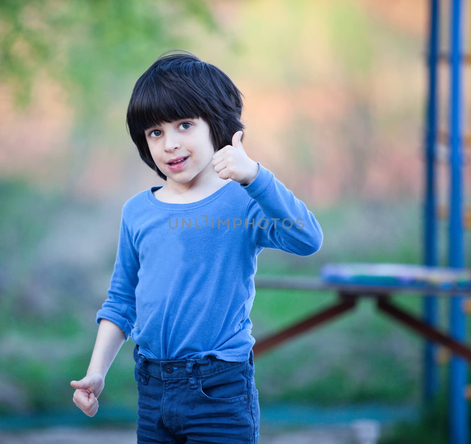 smiling black-haired boy in blue shirt showing a thumbs up