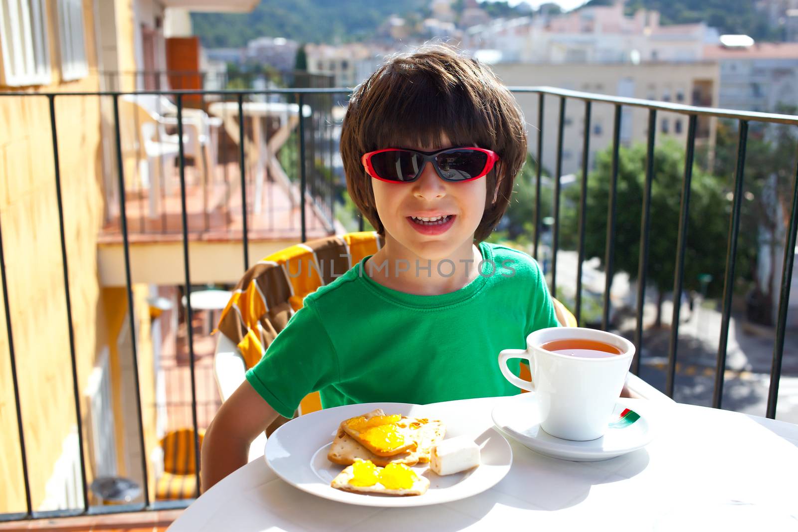 child in sunglasses breakfast on the terrace under the bright morning sun