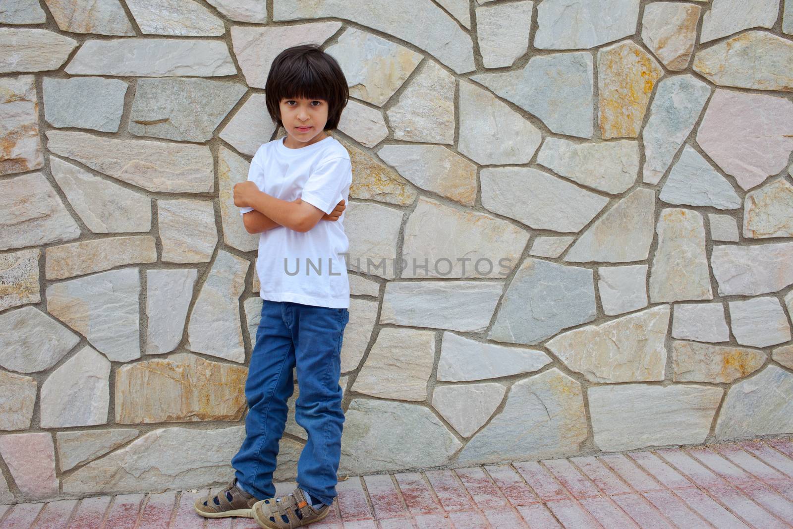 boy in a white shirt standing near the wall with masonry
