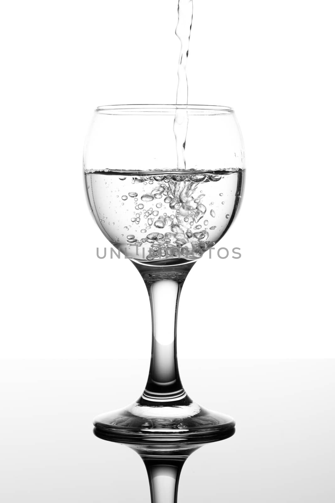 transparent glass with water pouring in on white background