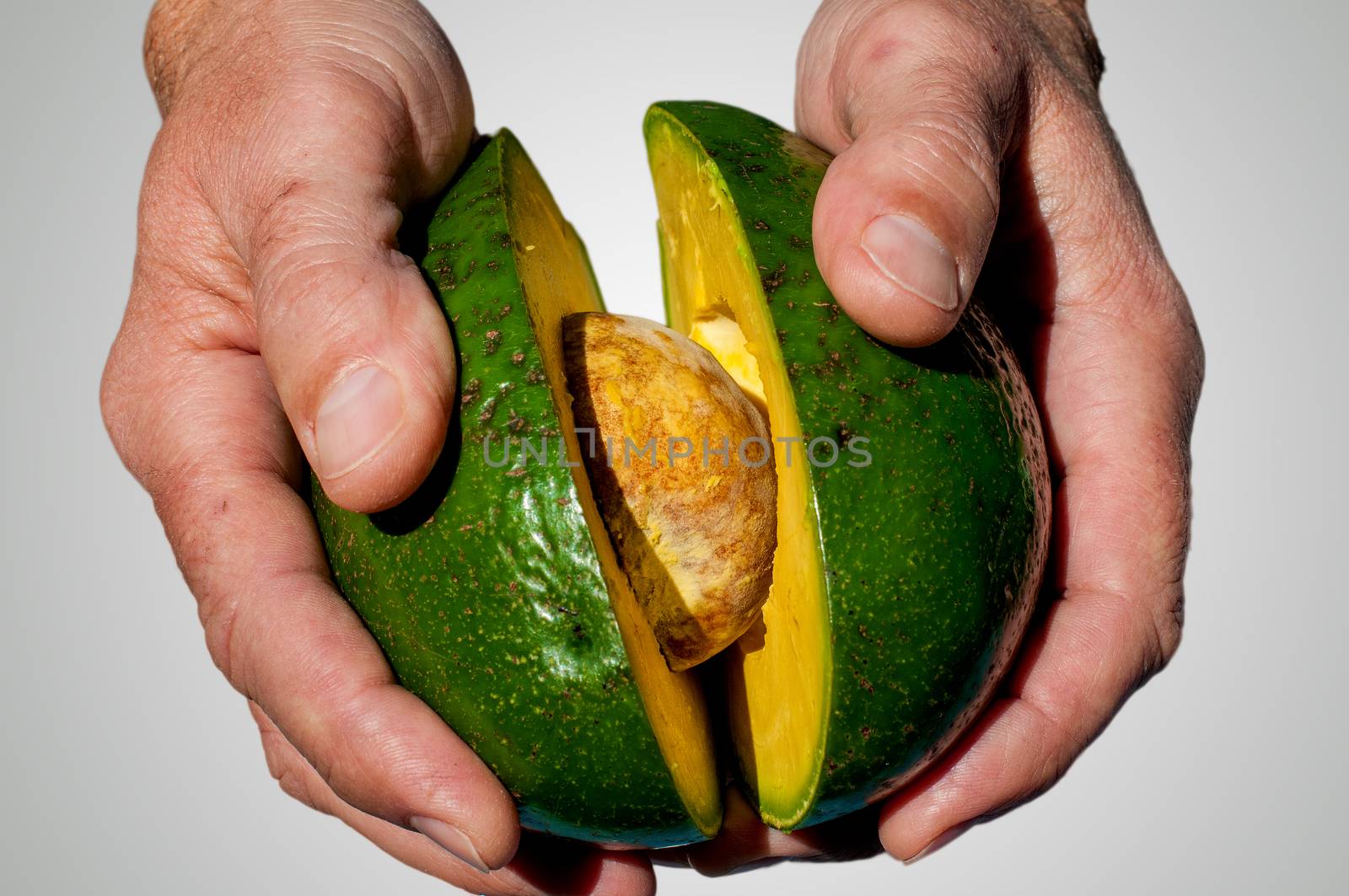 Hands with an open avocado in wich we can see the big seed