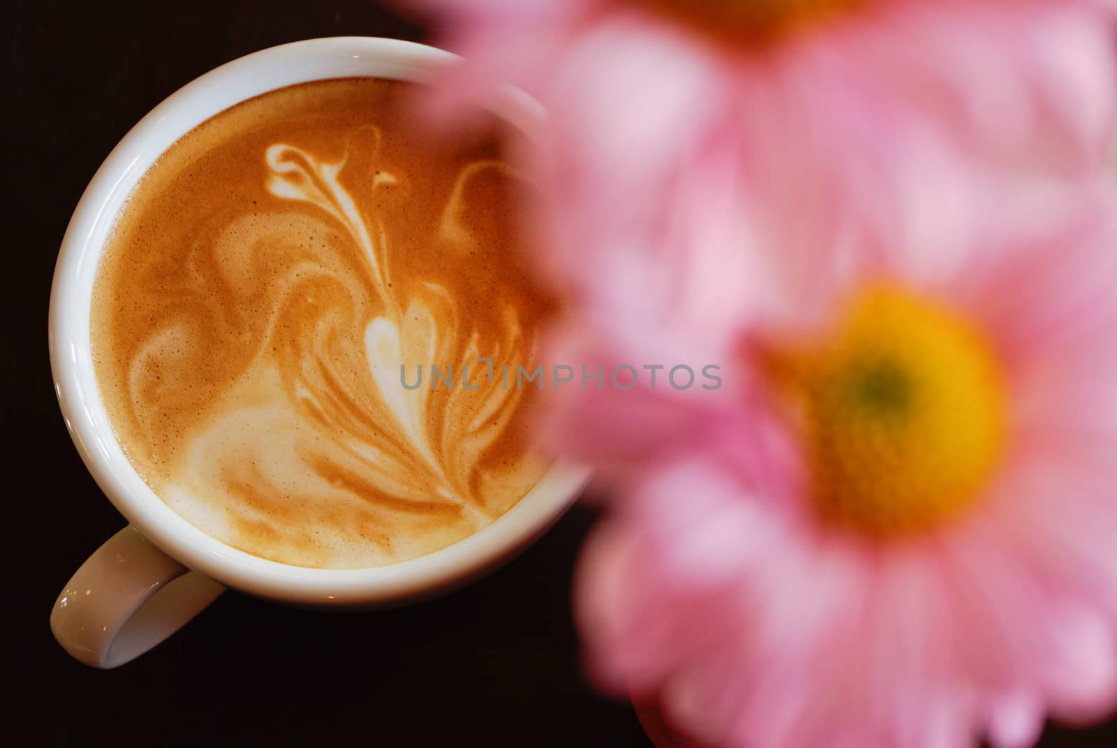 White cup of coffee with pink flower on black