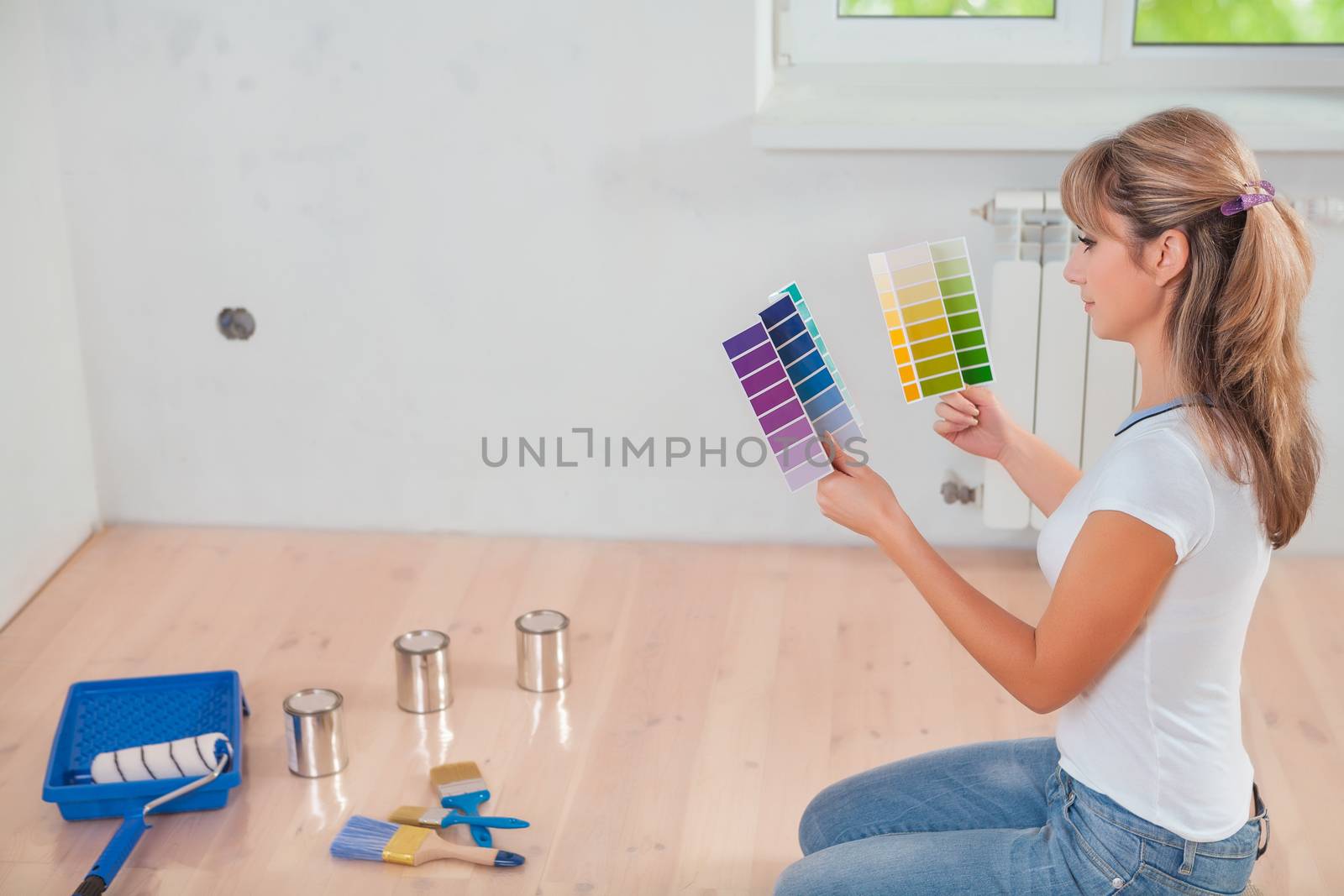beautiful female wearing working clothes sitting on wooden floor holding two color palettes and looking on it