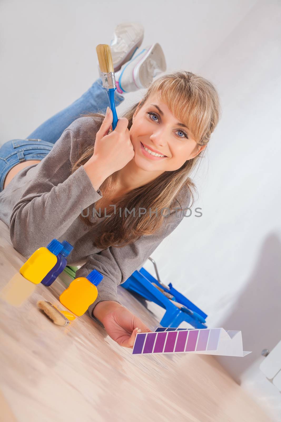 beautiful smiling woman lies on wooden floor holding paintbrush and color palette
