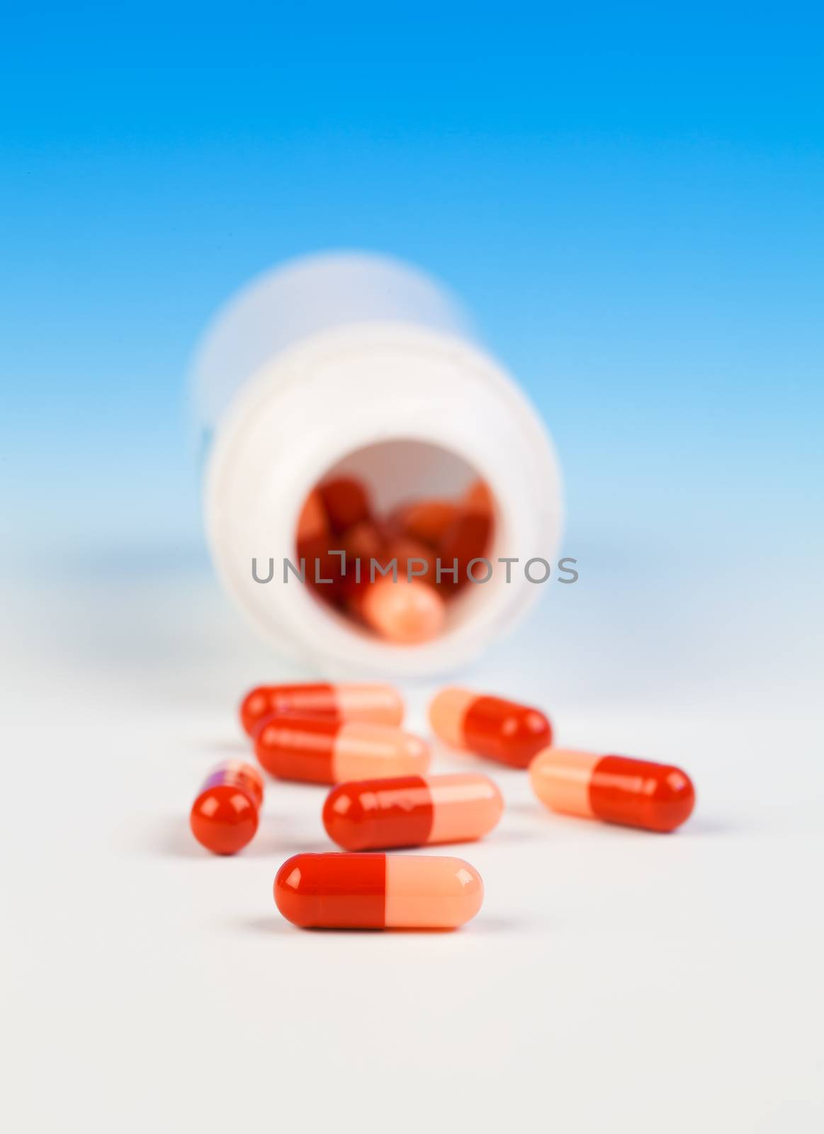 Pills spilling out of pill bottle isolated on blue (with sample text)